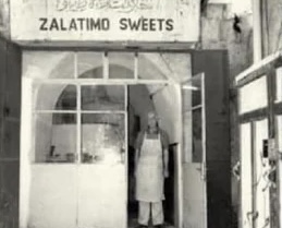Black-and-white photograph of the Zalatimo Sweets shopfront in Jerusalem's Old City, with a man in an apron standing in the doorway