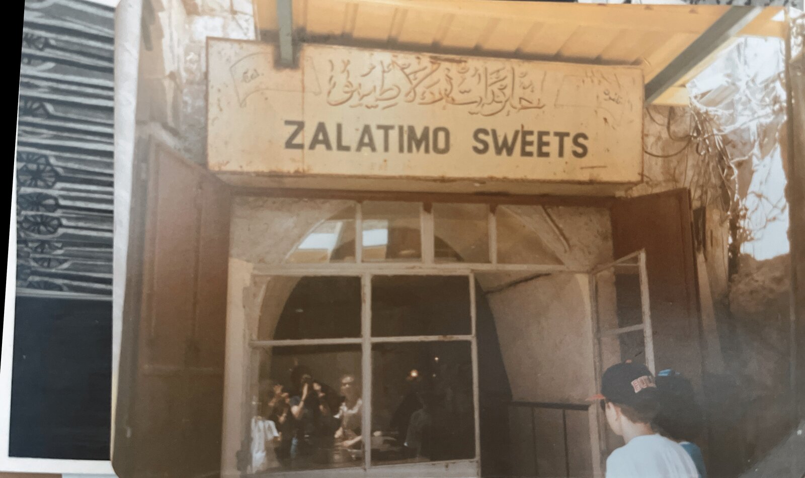 Color photograph of the Zalatimo Sweets sign above the open shop entrance, with customers inside