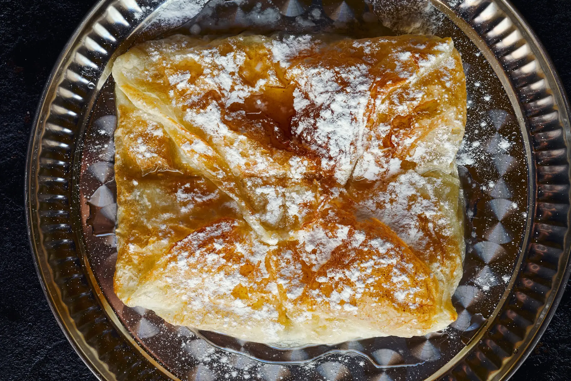 Mutabbaq — folded pastry dusted with powdered sugar on a silver tray